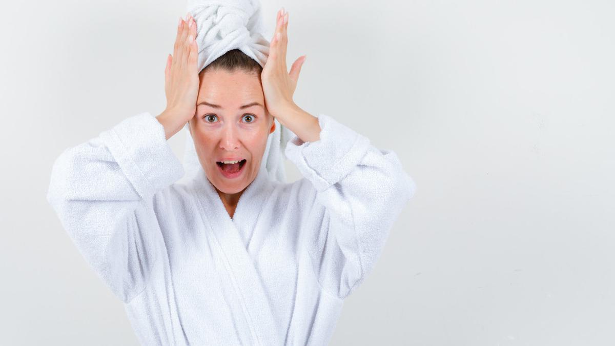 014692000 1692672388 Young Lady White Bathrobe Towel Holding Hands Head Looking Distressed Front View